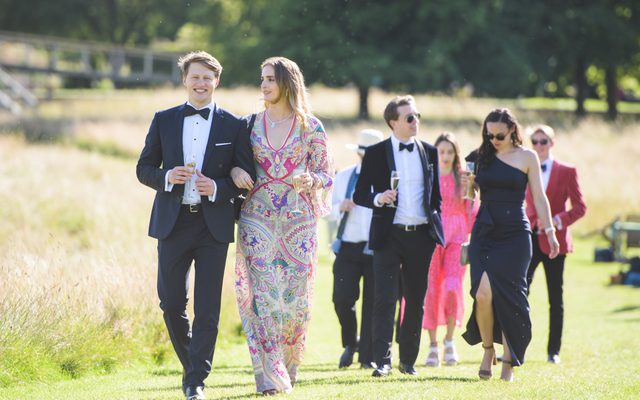A group of people walking in evening wear down a mown grass path