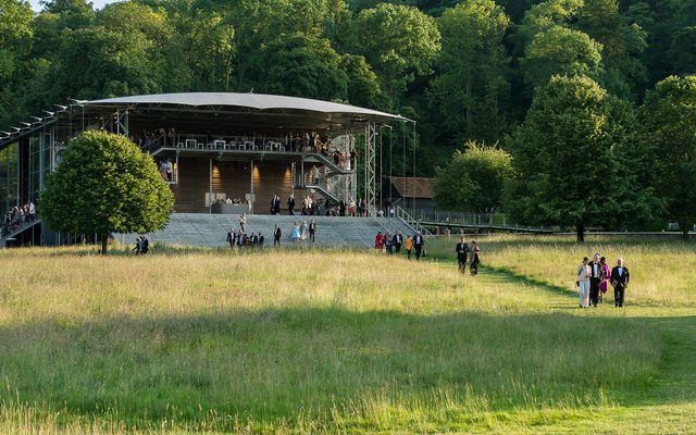 The Opera Pavilion at Wormsley, framed by lush green tress and with people meandering down the path from it.