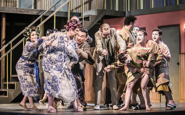 A fight between a group in hair curlers and silk dressing gowns and another group in pink and green striped fluffy dressing gown and white painted faces. An image from Garsington Opera's 2023 performance of 'Ariadne auf Naxos' by Strauss.