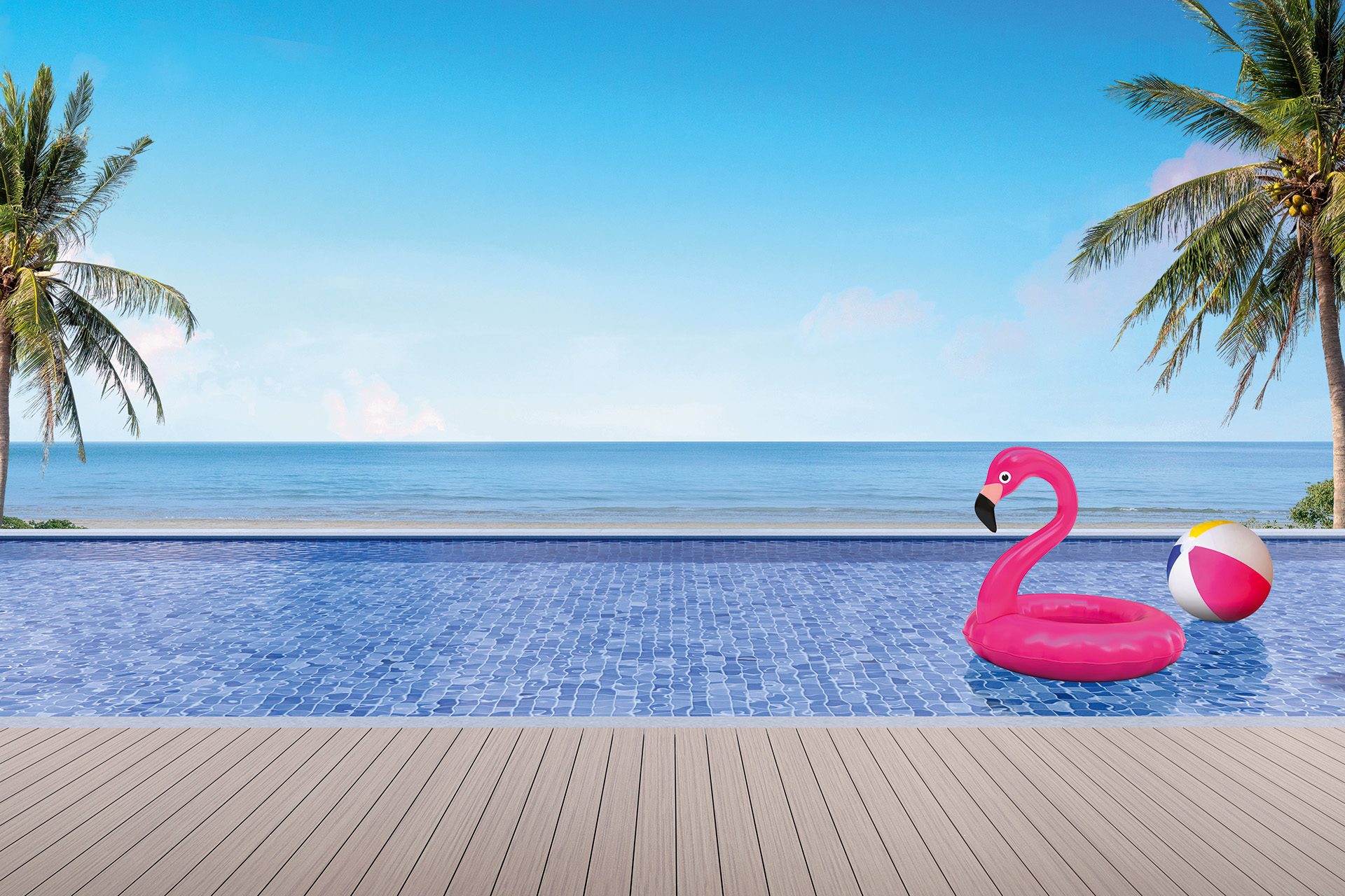 A pink inflatable flamingo swimming ring floats on a clear swimming pool against a beautiful, tropic beach backdrop.