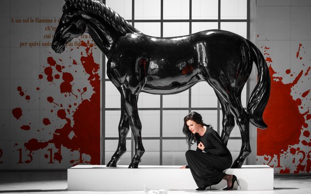 A woman crouches at the foot of a black horse statue.