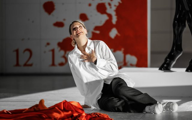 A woman in a white shirt and black trousers sits on the floor.
