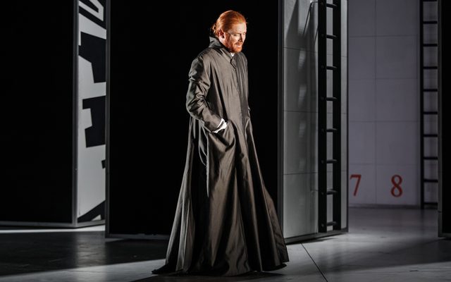 A ginger headed man in a long grey robe paces across.