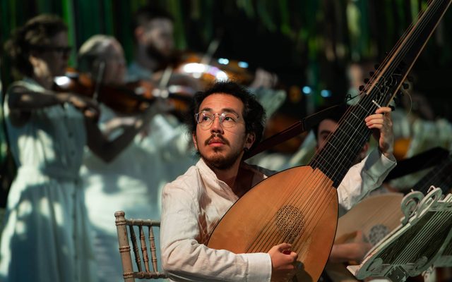 A man dressed in white plays a theorbo.
