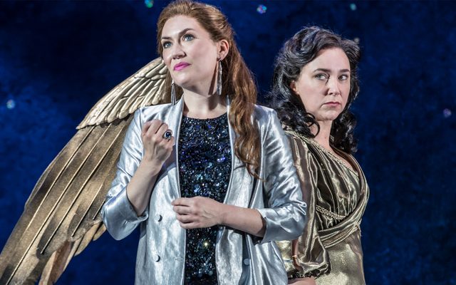 A woman dressed in gold with large gold wings gives a woman in a silver jacket side-eye.